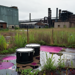 **Abandoned industrial site:**  "A derelict paint factory, showing colorful stains on the ground, scattered drums, and overgrown weeds. Focus on the signs of potential soil and groundwater contamination, with an ominous, slightly surreal atmosphere. Overcast lighting."